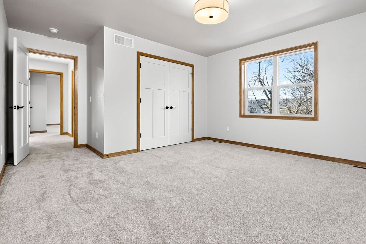 Spacious bedroom with carpet flooring, double closet, hallway entry, and large window in a Fox Cities home