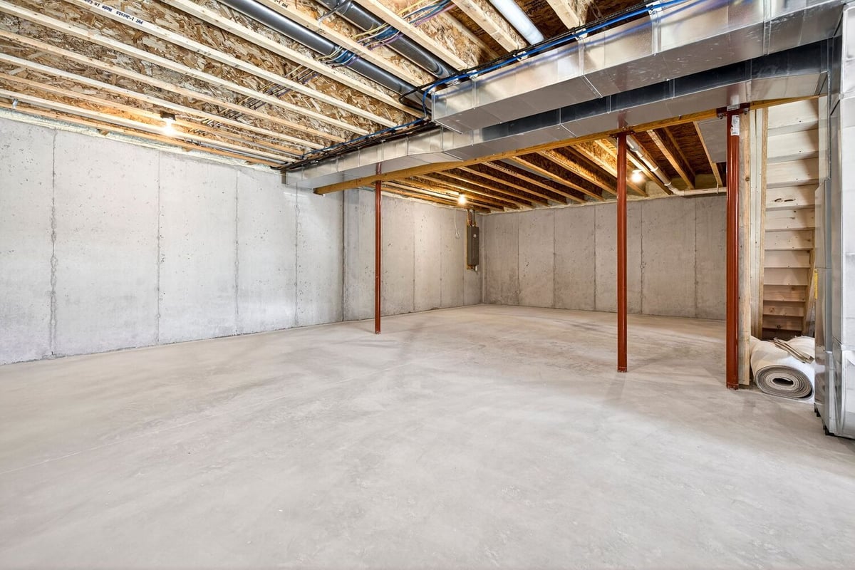 Unfinished basement with concrete floors, exposed beams, ductwork, and support posts in a Fox Cities home