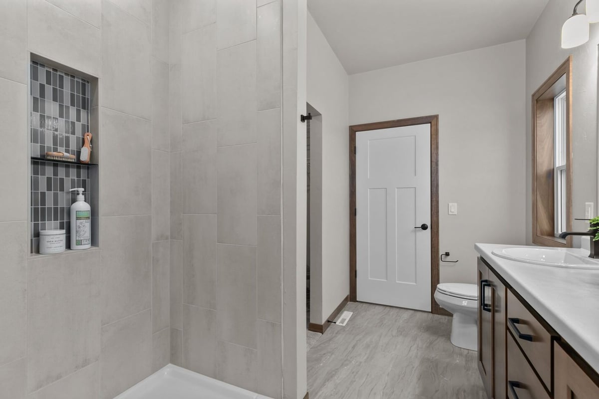 Tiled walk-in shower with built-in shelving in a custom bathroom by Midwest Design Homes in Appleton, WI