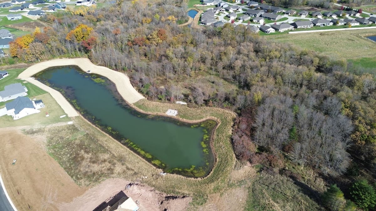 Aerial view of land for sale in De Pere, WI featuring pond frontage and surrounding trees near homes