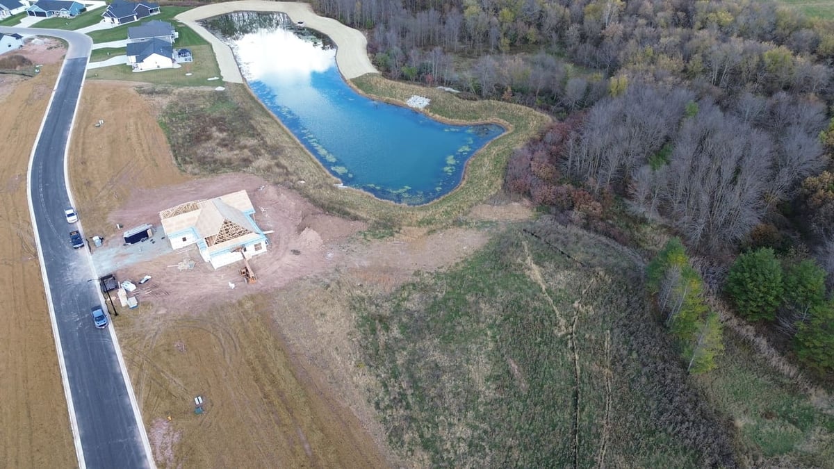 Aerial view of land for sale in De Pere, WI near pond, wooded area, and new home construction