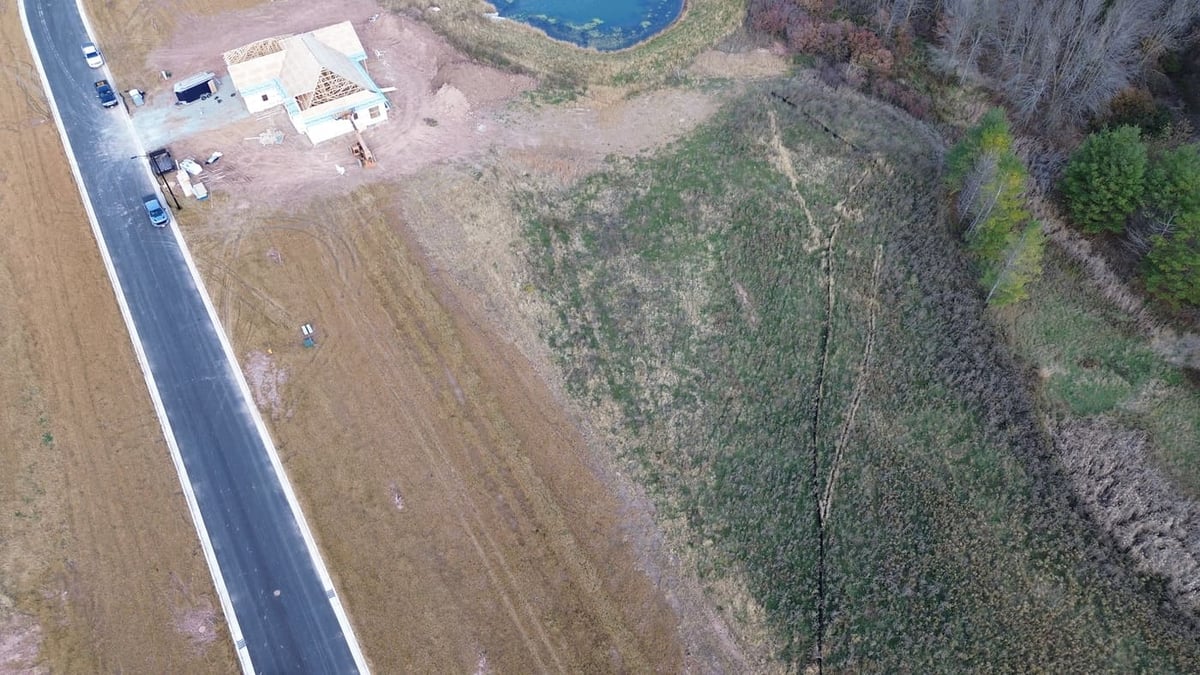 Overhead view of land for sale in De Pere, WI beside pond, trees, and paved roadway