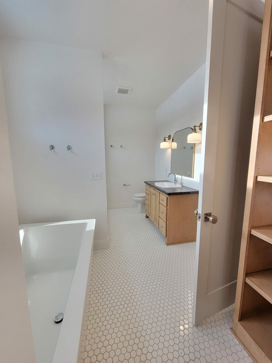 Bathroom with soaking tub, wood vanity, hex tile floor, and closet shelving, located in the Fox Cities