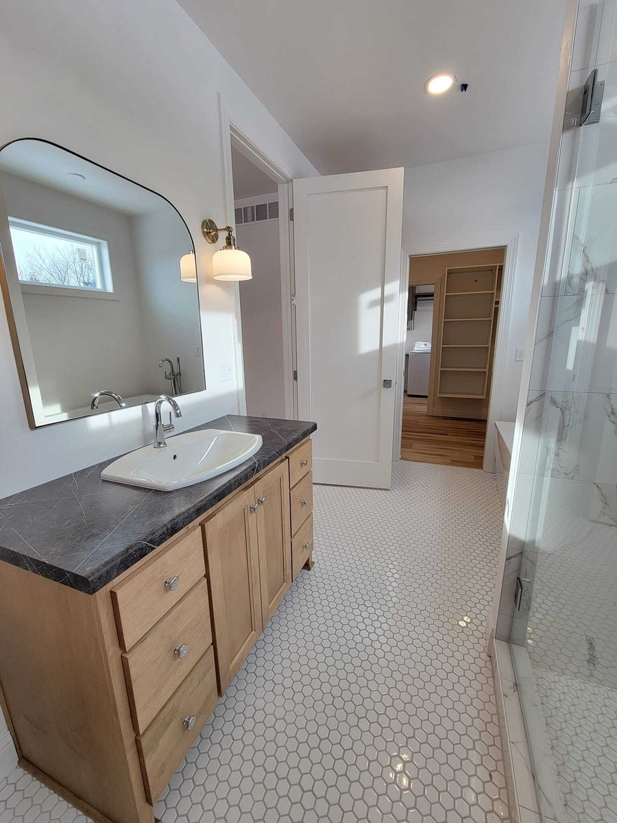 Bathroom with wood vanity, vessel sink, hex tile floor, glass shower, and walk-in closet beyond, located in the Fox Cities