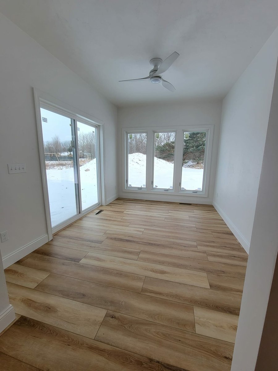 Bright sunroom with wood-look flooring, ceiling fan, sliding patio door, and large windows overlooking snowy yard in a Fox Cities home