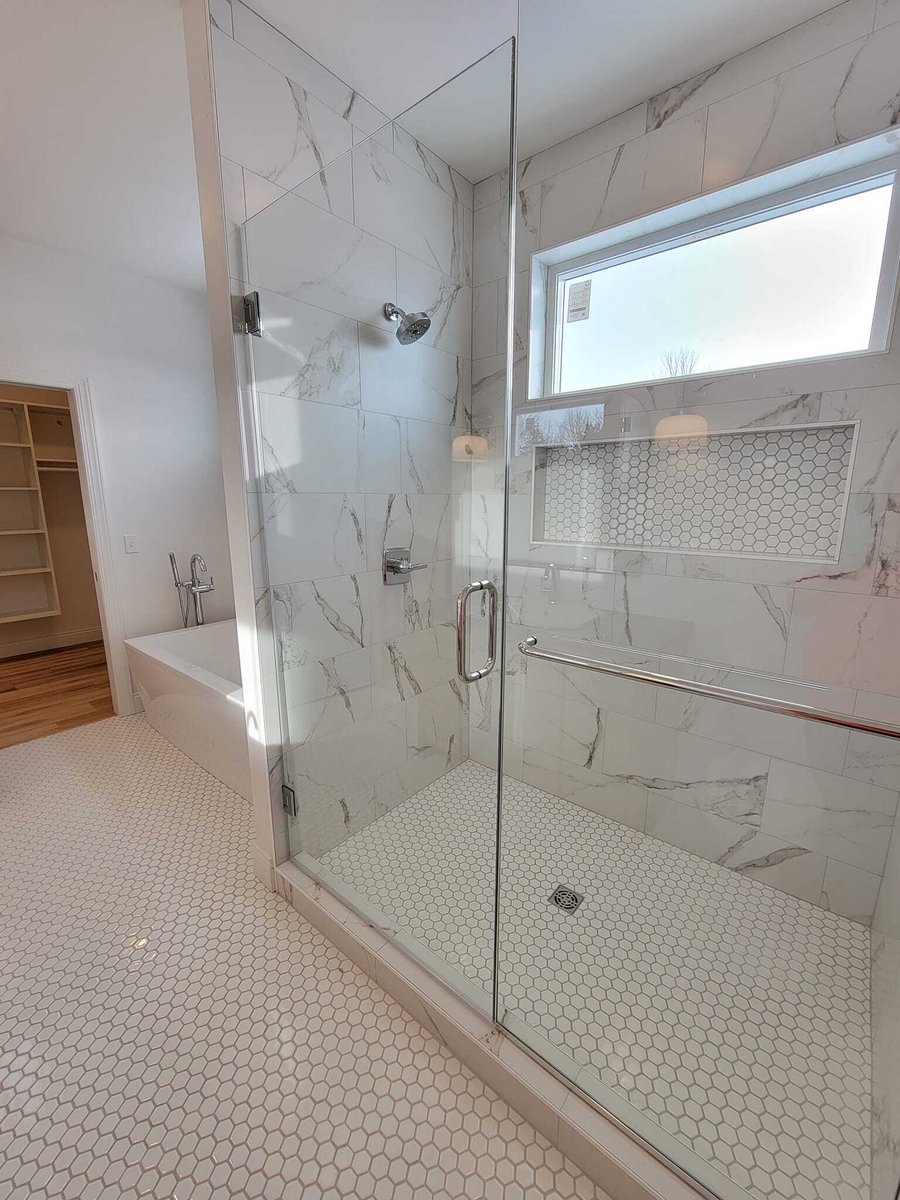 Glass walk-in shower with marble-look tile, hex floor tile, and niche window in a Fox Cities home bathroom