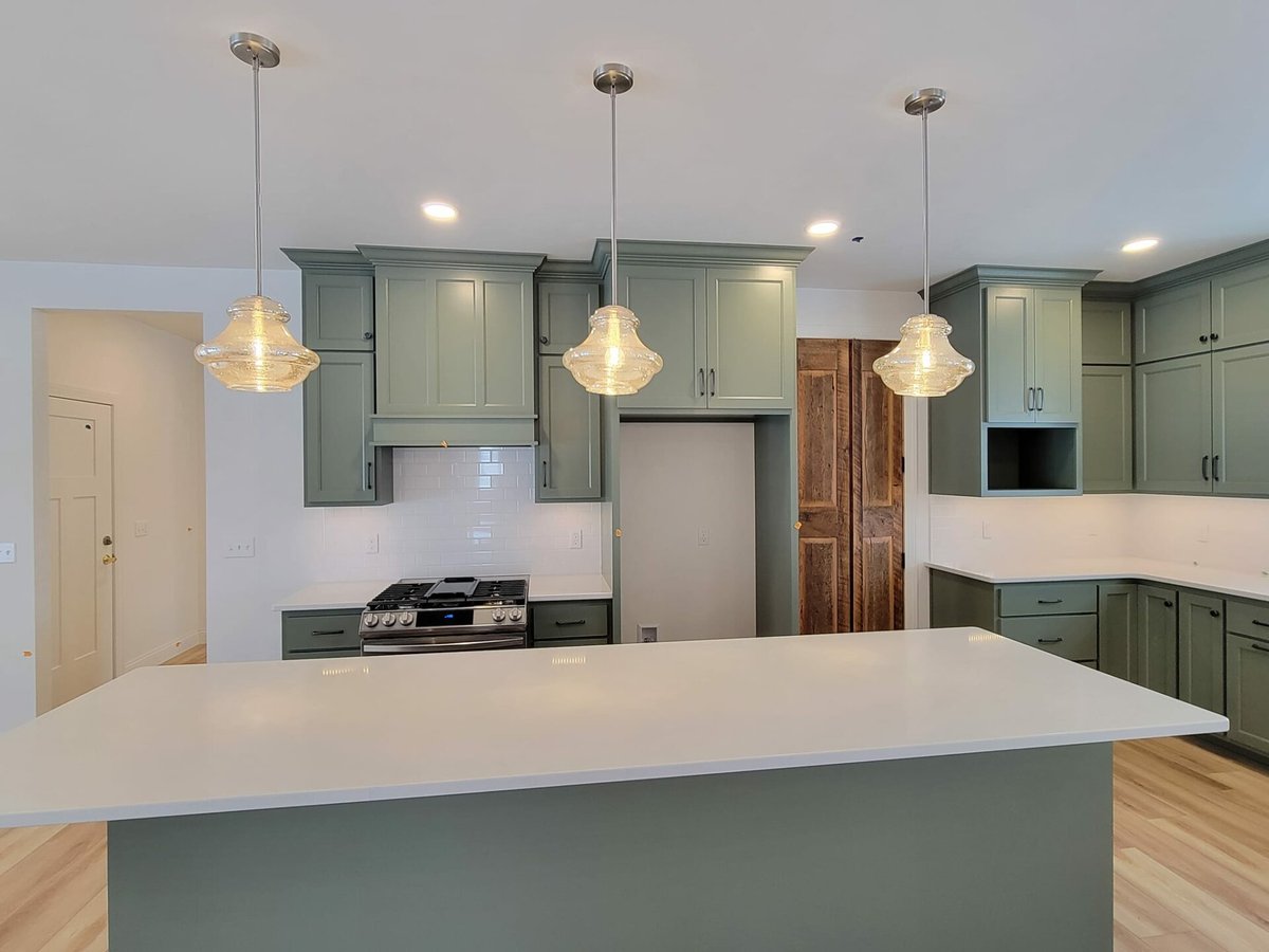 Kitchen with green cabinetry, white quartz island, pendant lighting, and stainless range, located in the Fox Cities