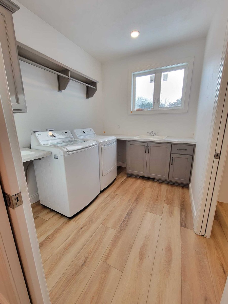 Laundry room with washer, dryer, sink, and cabinets, featuring wood-look flooring and window, located in the Fox Cities