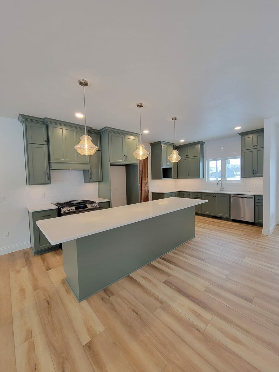 Modern kitchen with green cabinets, large island, pendant lighting, and wood floors, located in the Fox Cities