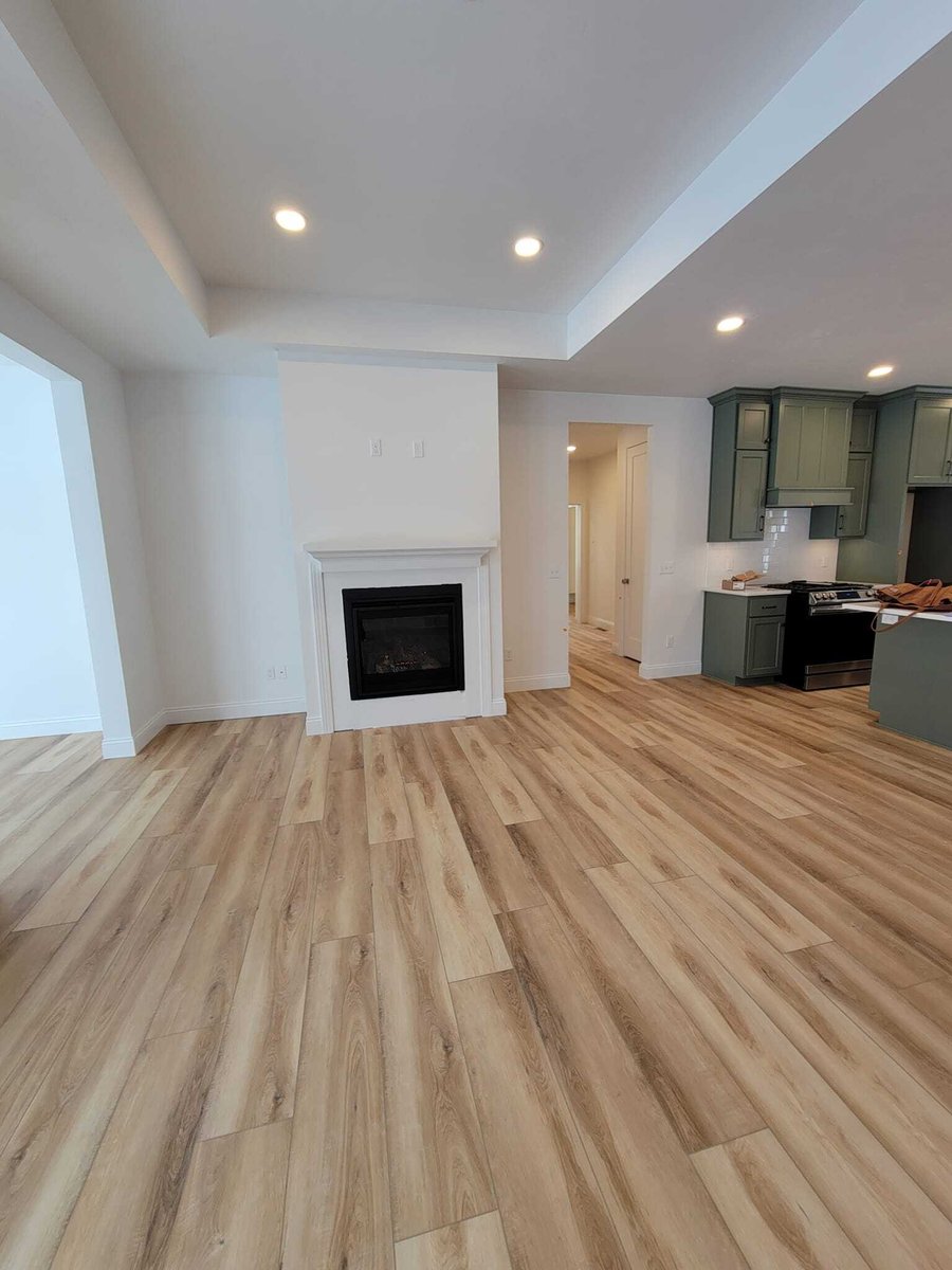 Open living area with light wood floors, tray ceiling, fireplace, and view into kitchen, located in the Fox Cities