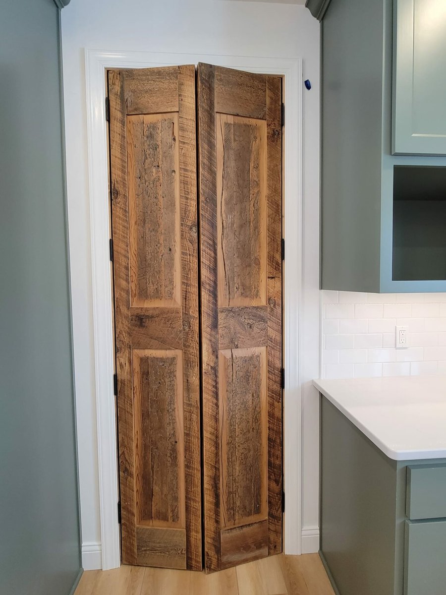 Rustic wood double pantry doors set between sage cabinets and white trim in a kitchen, located in the Fox Cities