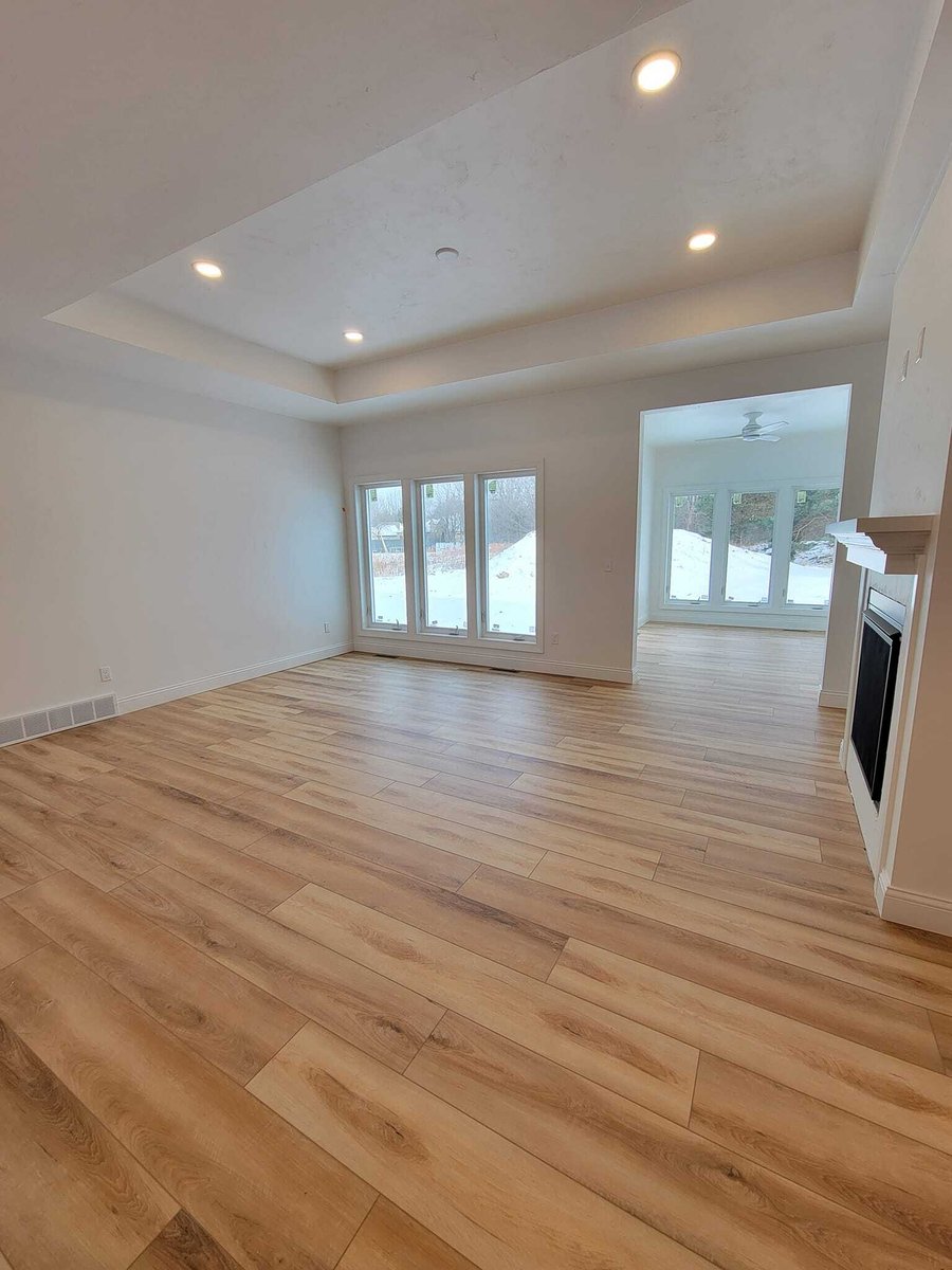 Spacious living room with tray ceiling, wood floors, and large windows overlooking snow, located in the Fox Cities
