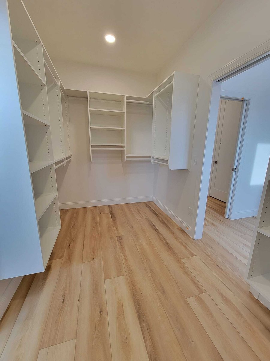 Walk-in closet with built-in white shelving and light wood floors, located in the Fox Cities