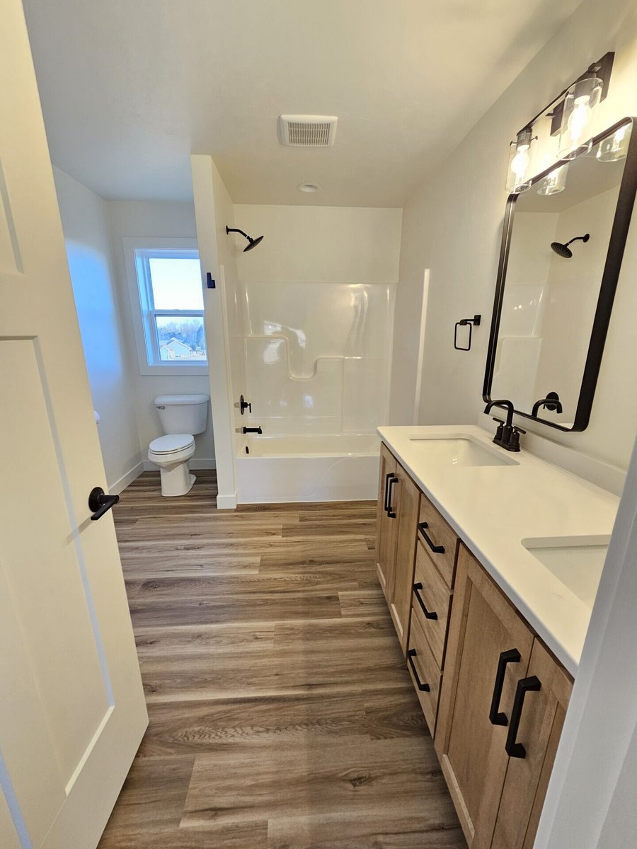 Bathroom with tubshower combo, wood vanity, white countertop, black fixtures, and vinyl flooring in a Fox Cities home
