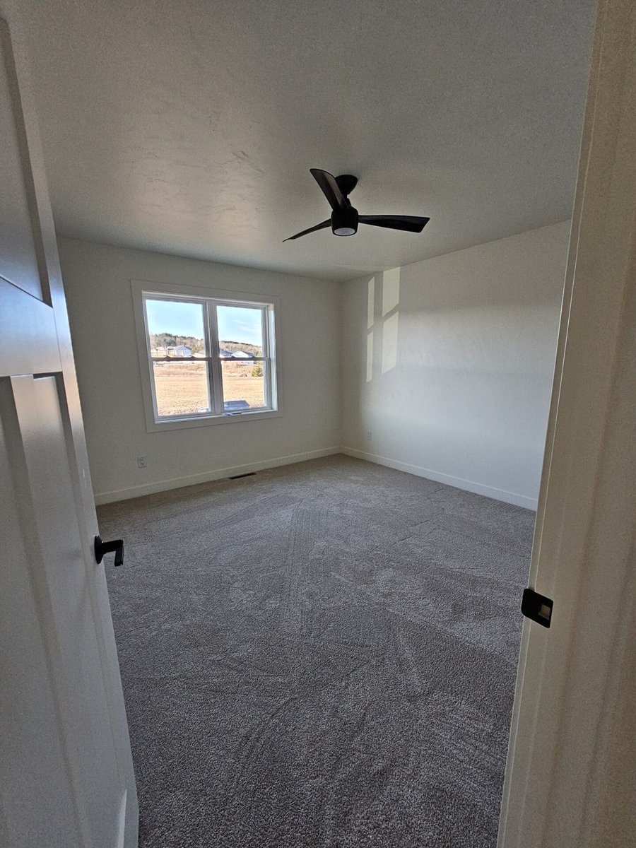 Empty bedroom with carpet, ceiling fan, and window letting in natural light in a Fox Cities home