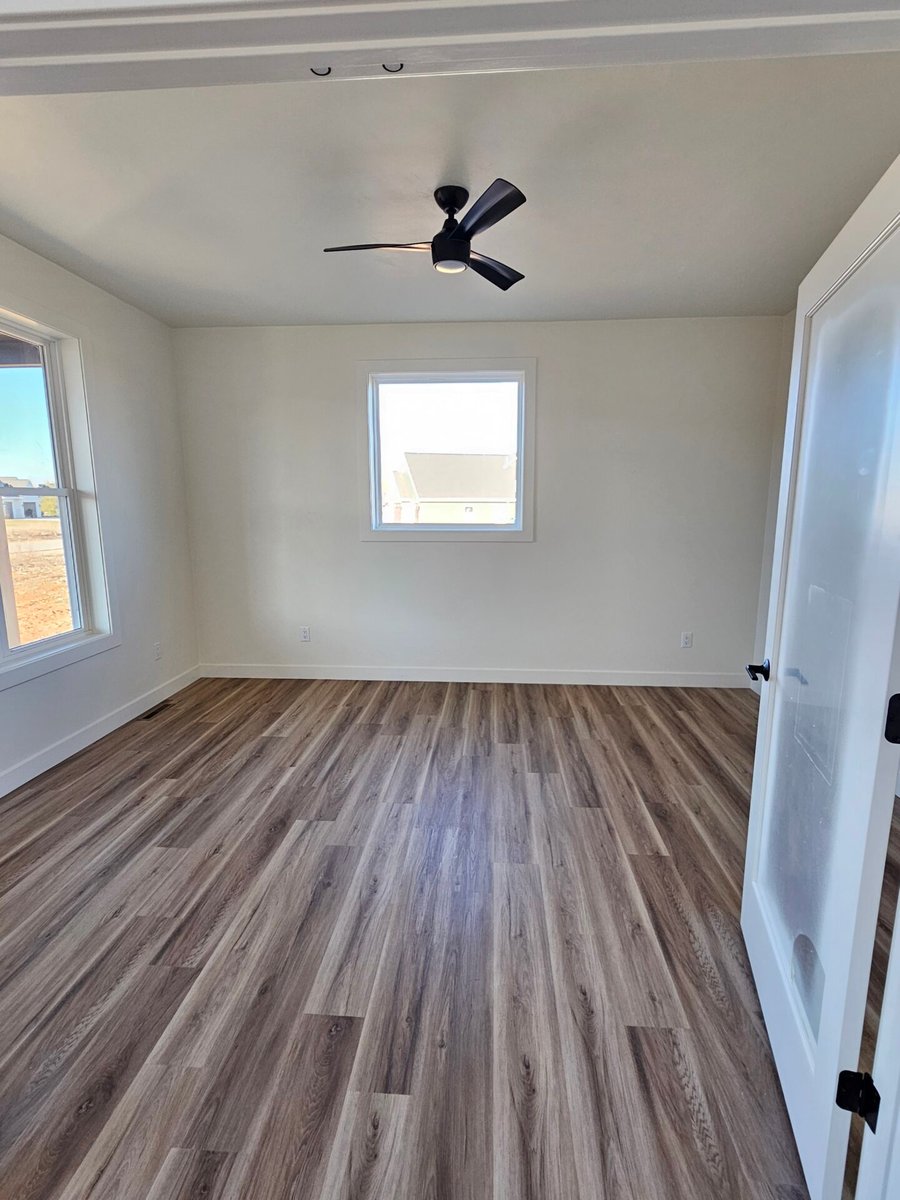 Empty room with wood-look flooring, ceiling fan, and window bringing in natural light in a Fox Cities home
