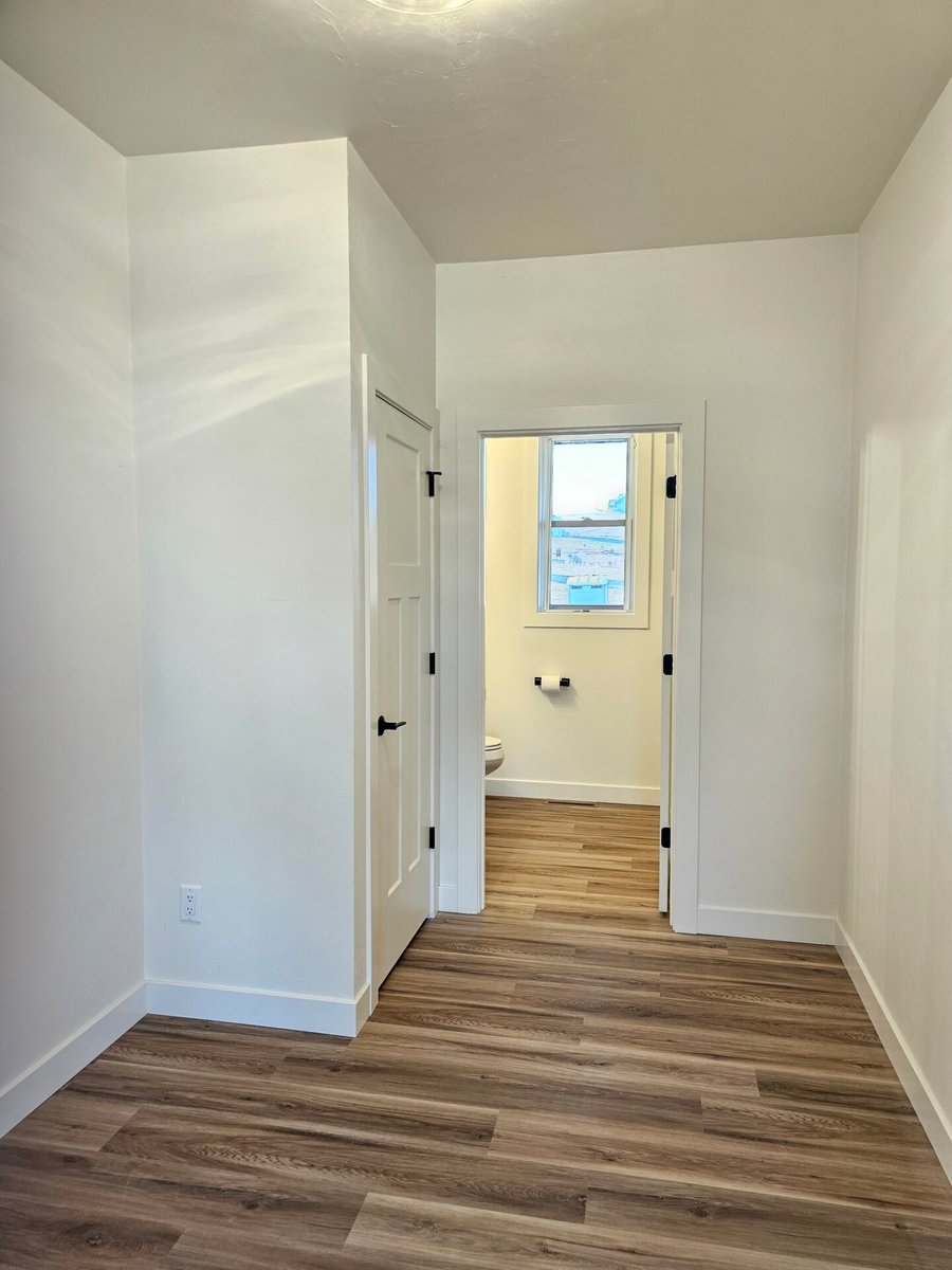 Hallway with wood-look flooring and white walls leading to a bathroom, located in a Fox Cities home