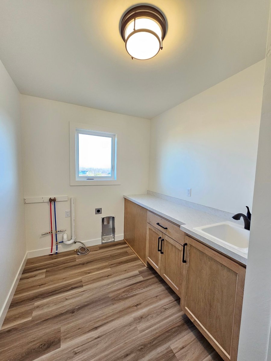 Laundry room with wood cabinets, quartz counter, utility sink, and vinyl flooring in a Fox Cities home