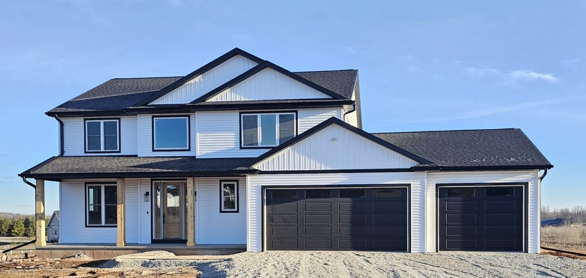 New two-story home exterior with white siding, black garage doors, and gravel drive in the Fox Cities