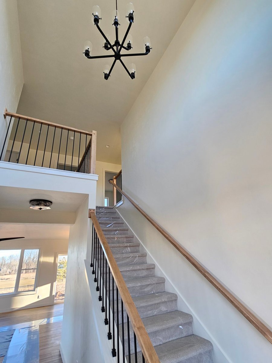 Open stairway with wood handrail, black balusters, carpeted steps, and modern chandelier in a Fox Cities home