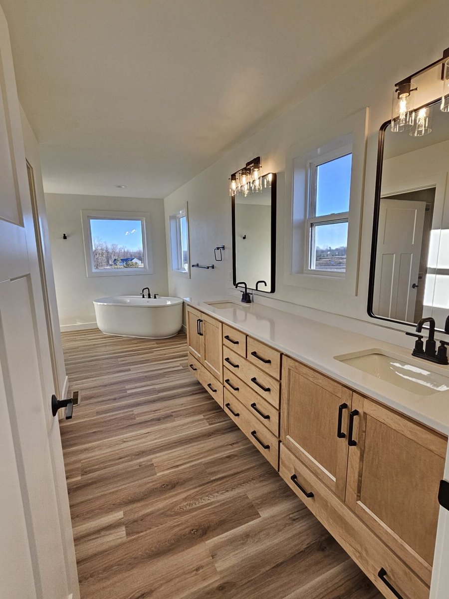 Primary bathroom with double vanity, modern mirrors, freestanding tub, and wood-look flooring in the Fox Cities