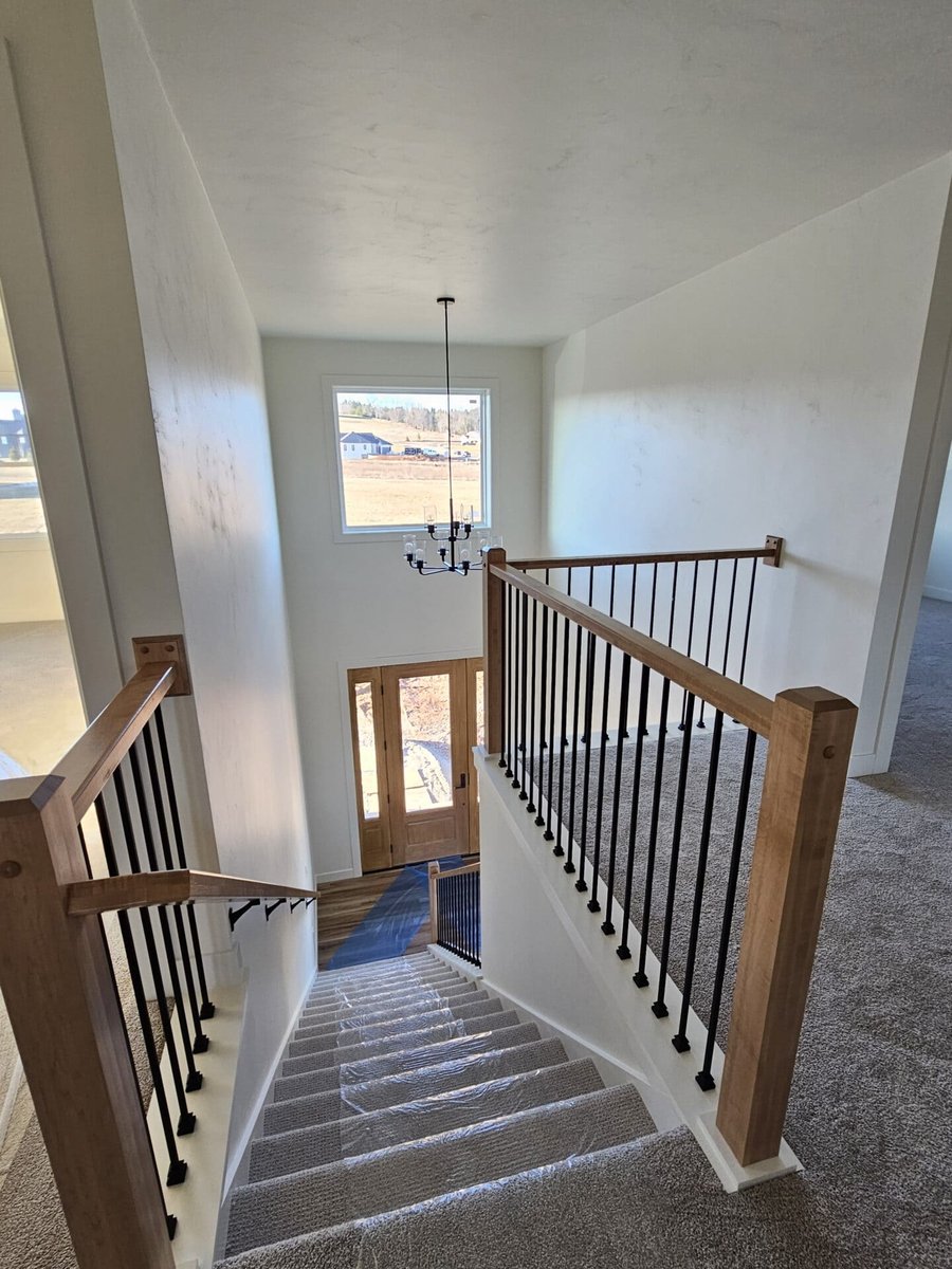 Staircase interior with wood handrails, black balusters, carpeted steps, and entry view in a Fox Cities home