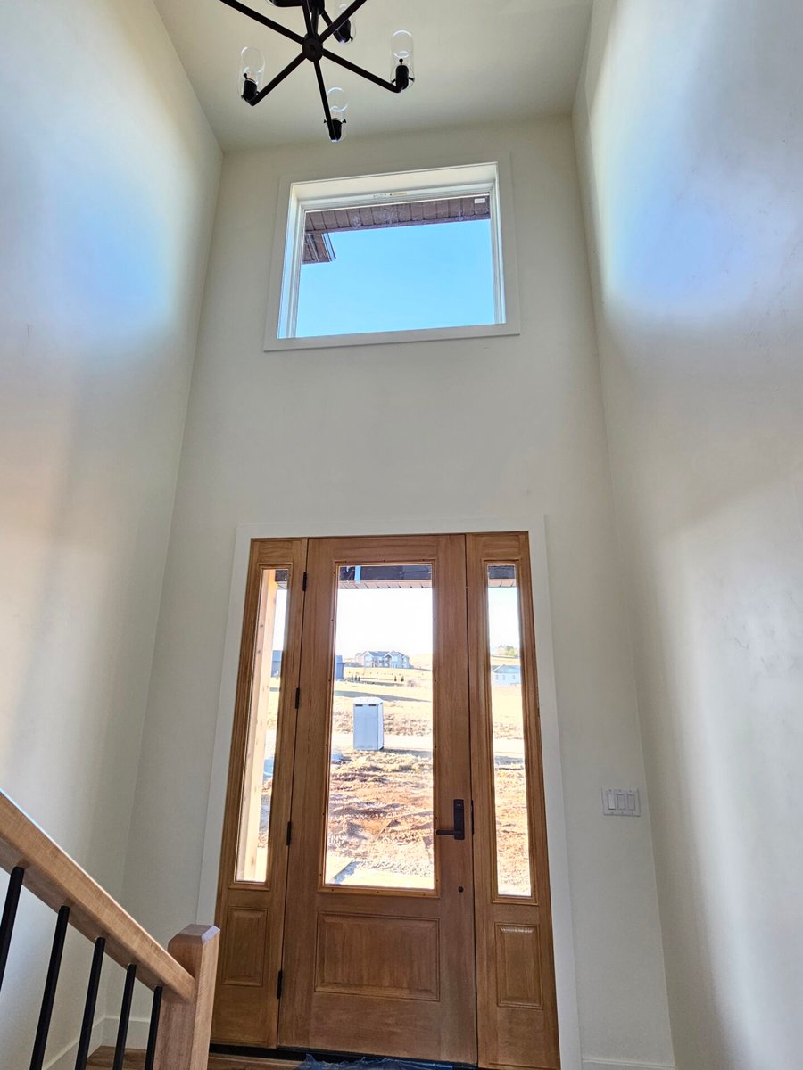 Two-story entryway with wood front door, tall window, and modern chandelier, located in the Fox Cities