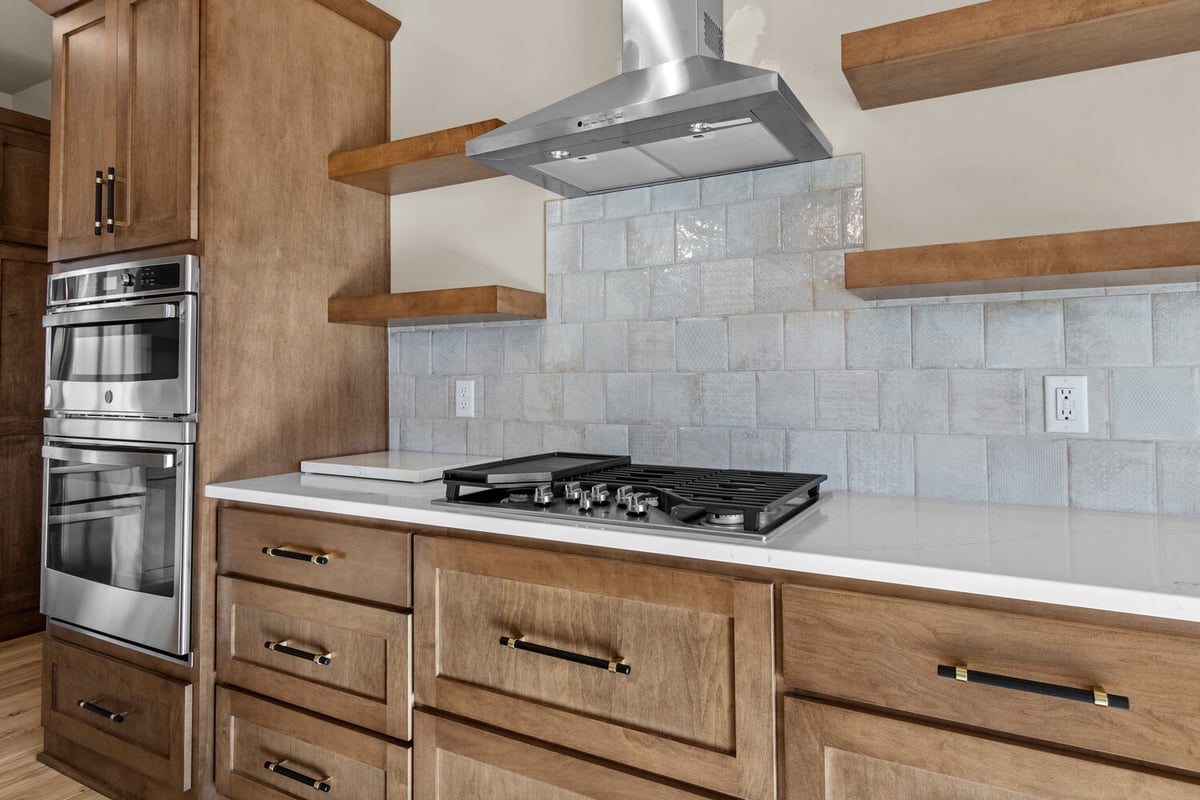 Kitchen cooktop with backsplash and wood shelves in Bellevue, WI custom home
