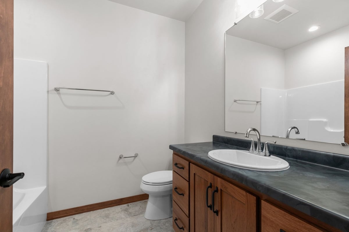 Full bath with wood vanity and black counter by Midwest Design Homes, Kaukauna, WI