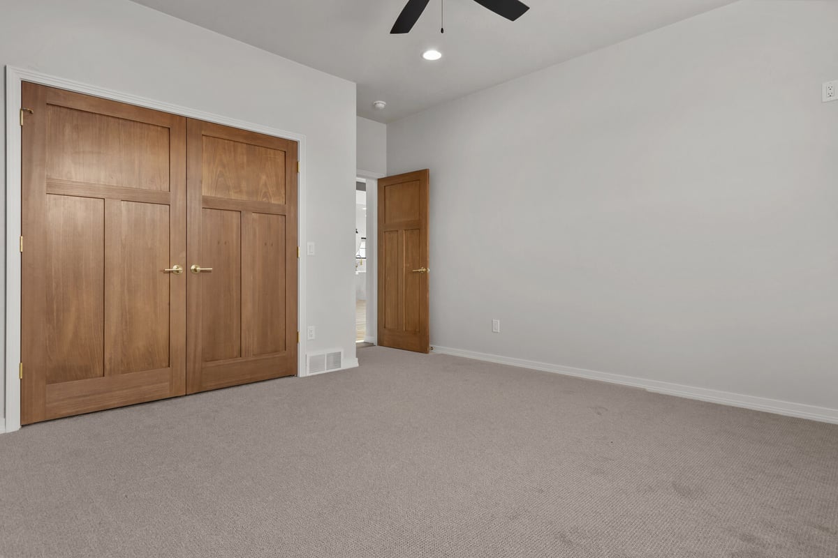 Bedroom with ceiling fan and wood closet doors by Midwest Design Homes in Fremont, WI