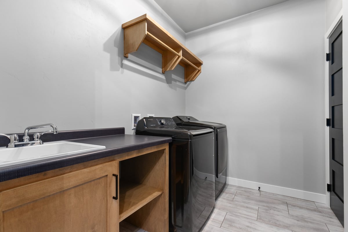 Bright laundry space with utility sink and black appliances by Midwest Design Homes