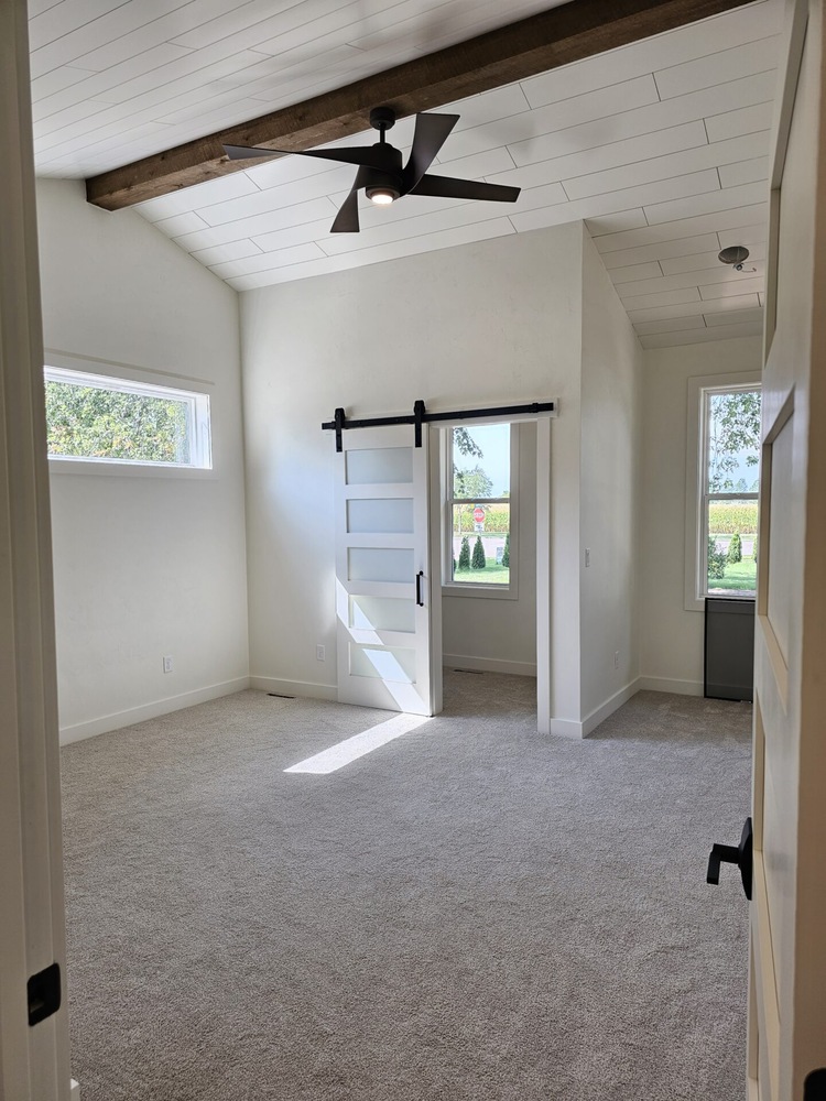 Modern bedroom with carpet and wood beam ceiling in Kaukauna by Midwest Design Homes