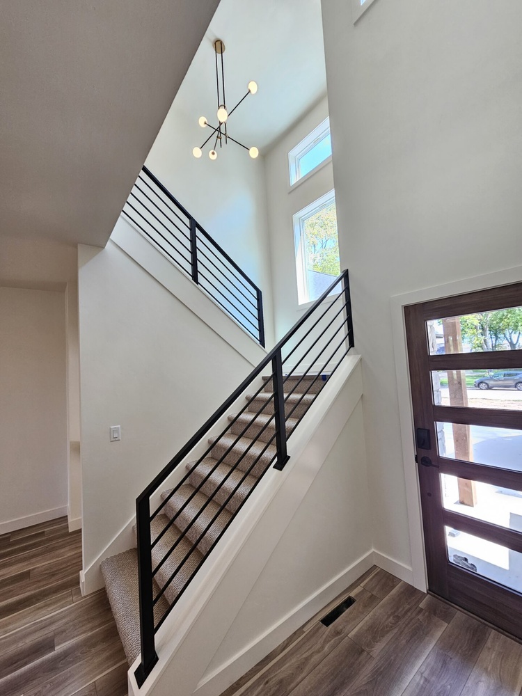 Staircase with modern railing and chandelier in Kaukauna home by Midwest Design Homes