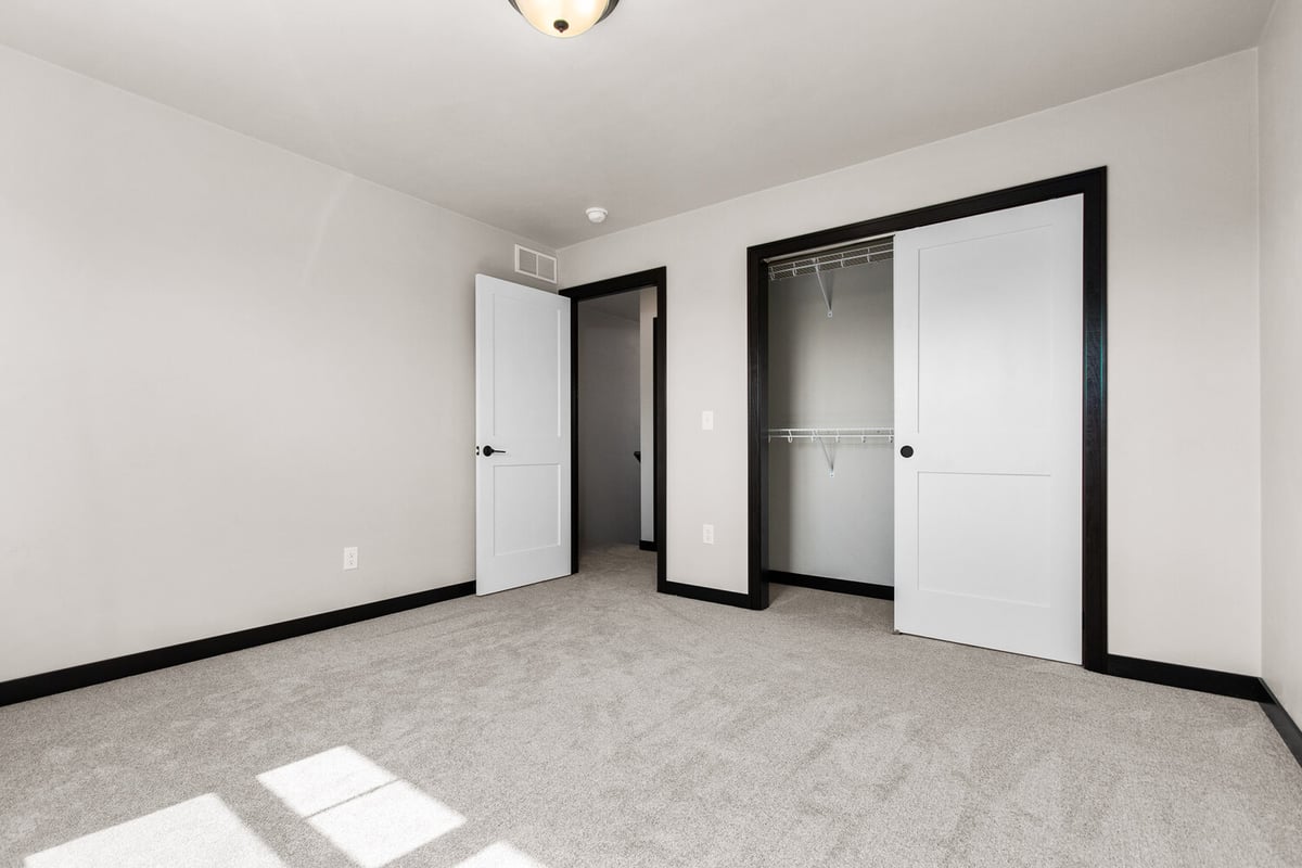 Empty bedroom with large window and double closet doors by Midwest Design Homes