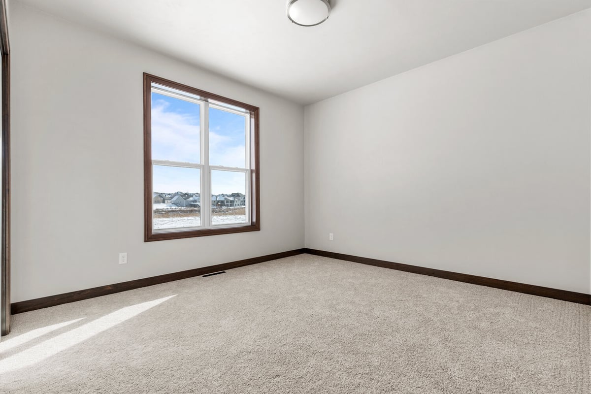 Simple guest room with soft carpet and big window in Kaukauna home by Midwest Design Homes