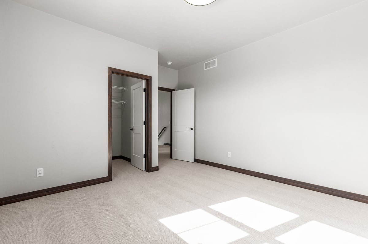 Empty carpeted bedroom in Wisconsin custom home by Midwest Design Homes with open doors