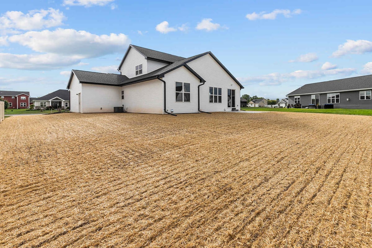 Wide backyard view of Wisconsin custom home by Midwest Design Homes with straw-covered lawn