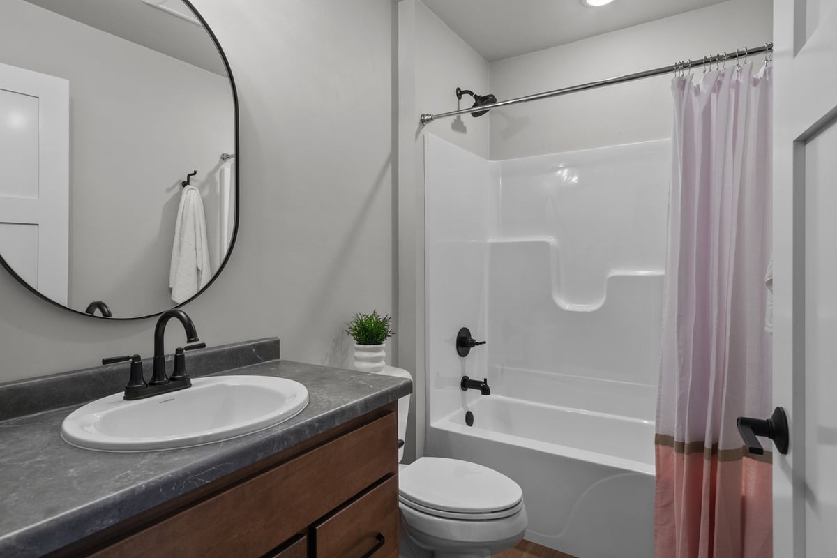 Compact bathroom with tub and round mirror in a Kaukauna, WI custom home by Midwest Design Homes