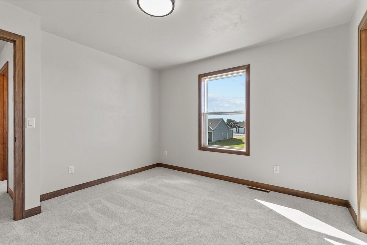 Carpeted bedroom with bright window in Wisconsin custom home by Midwest Design Homes