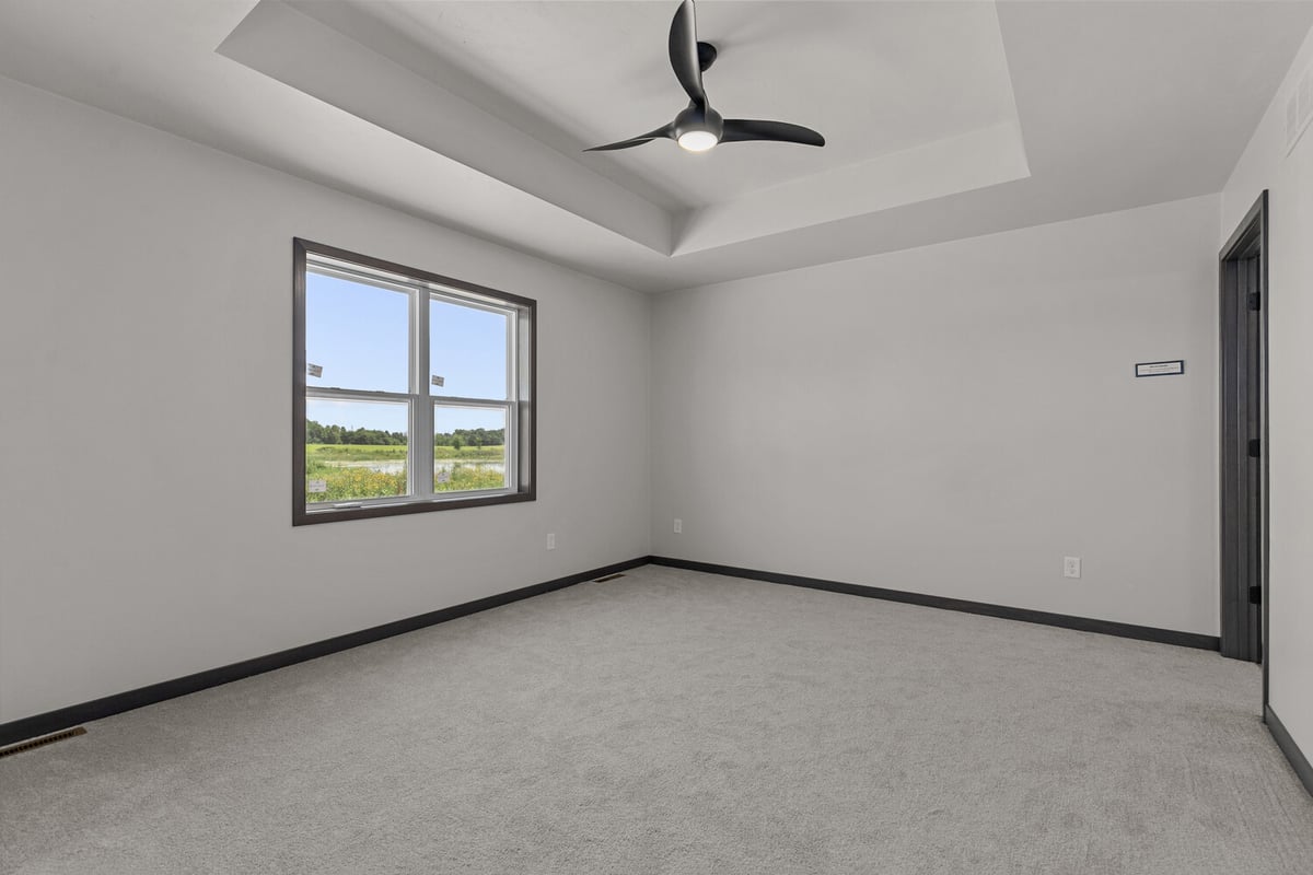 Primary bedroom with tray ceiling and large window in WI home by Midwest Design Homes