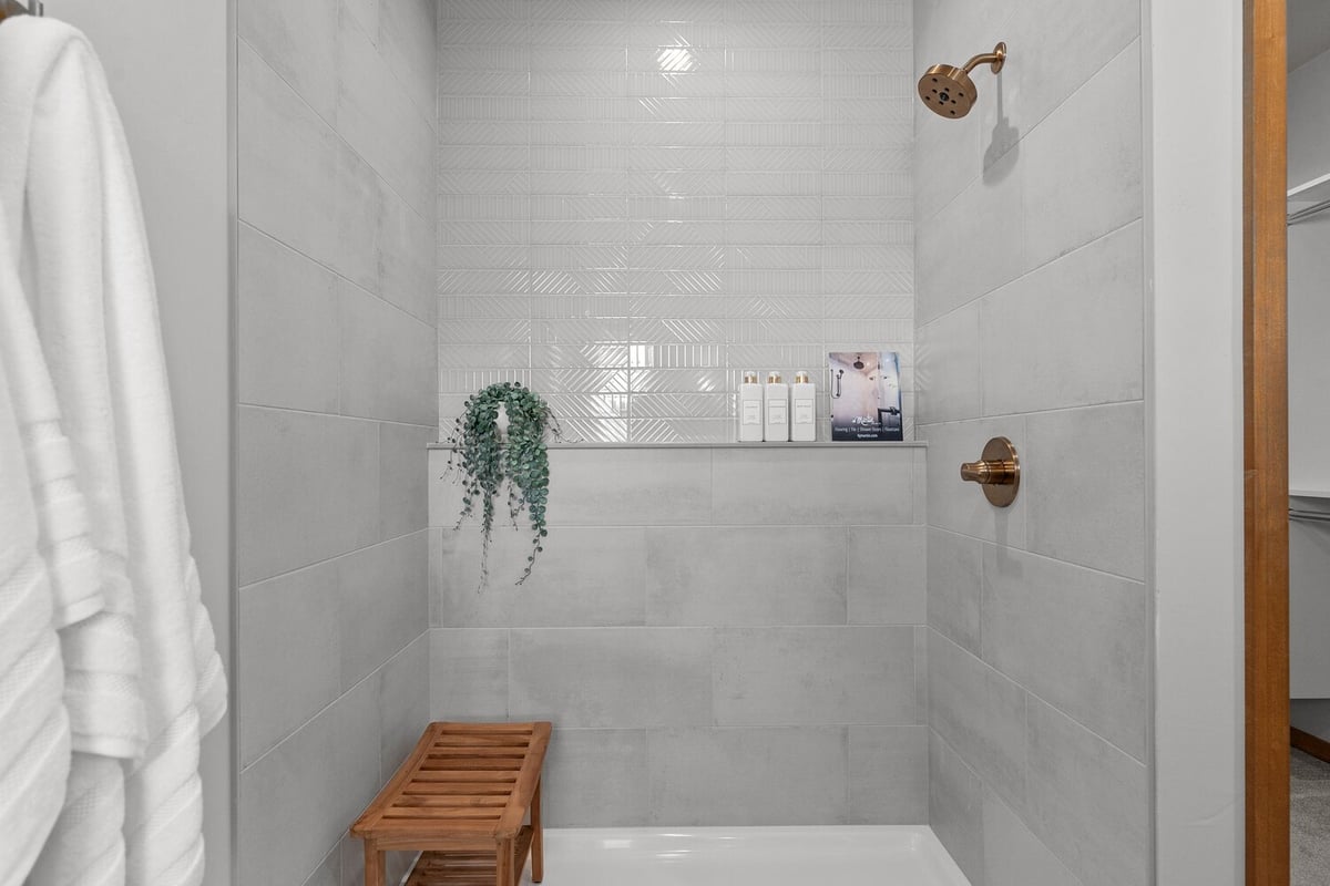 Shower with wood bench and textured wall tile by Midwest Design Homes in Lawrence WI
