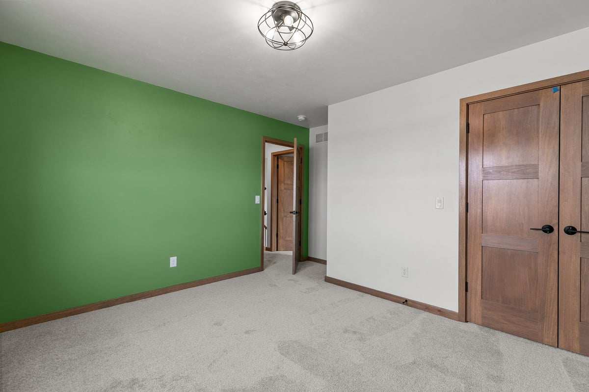 Bedroom with green accent wall, plush carpet, and wood trim in a modern Appleton, WI home