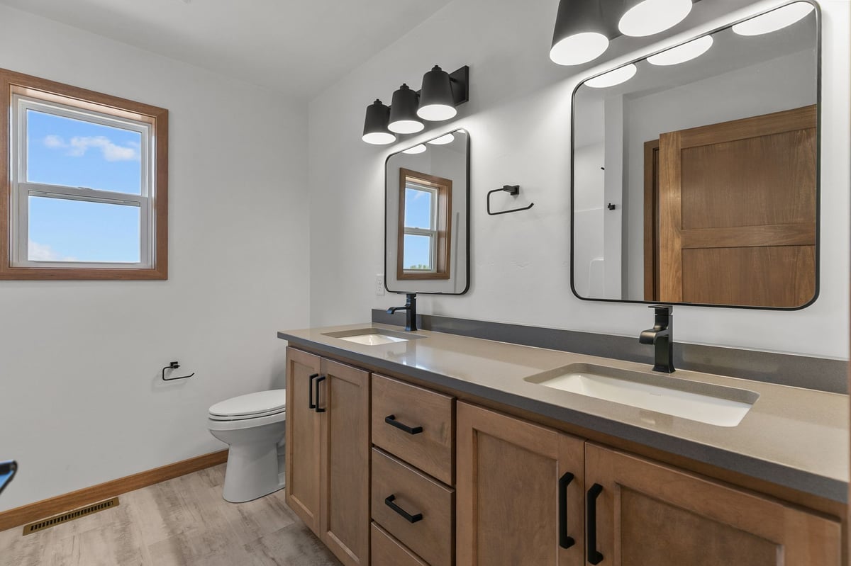 Bright bathroom with double sinks, wood cabinetry, and black fixtures in Appleton, WI