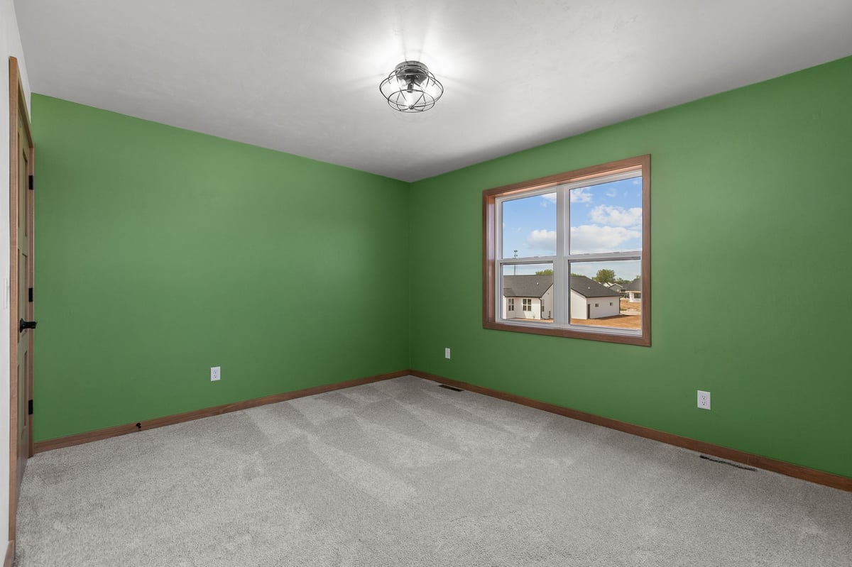 Bright bedroom with green walls, soft carpet, and large window in a new Appleton, WI home