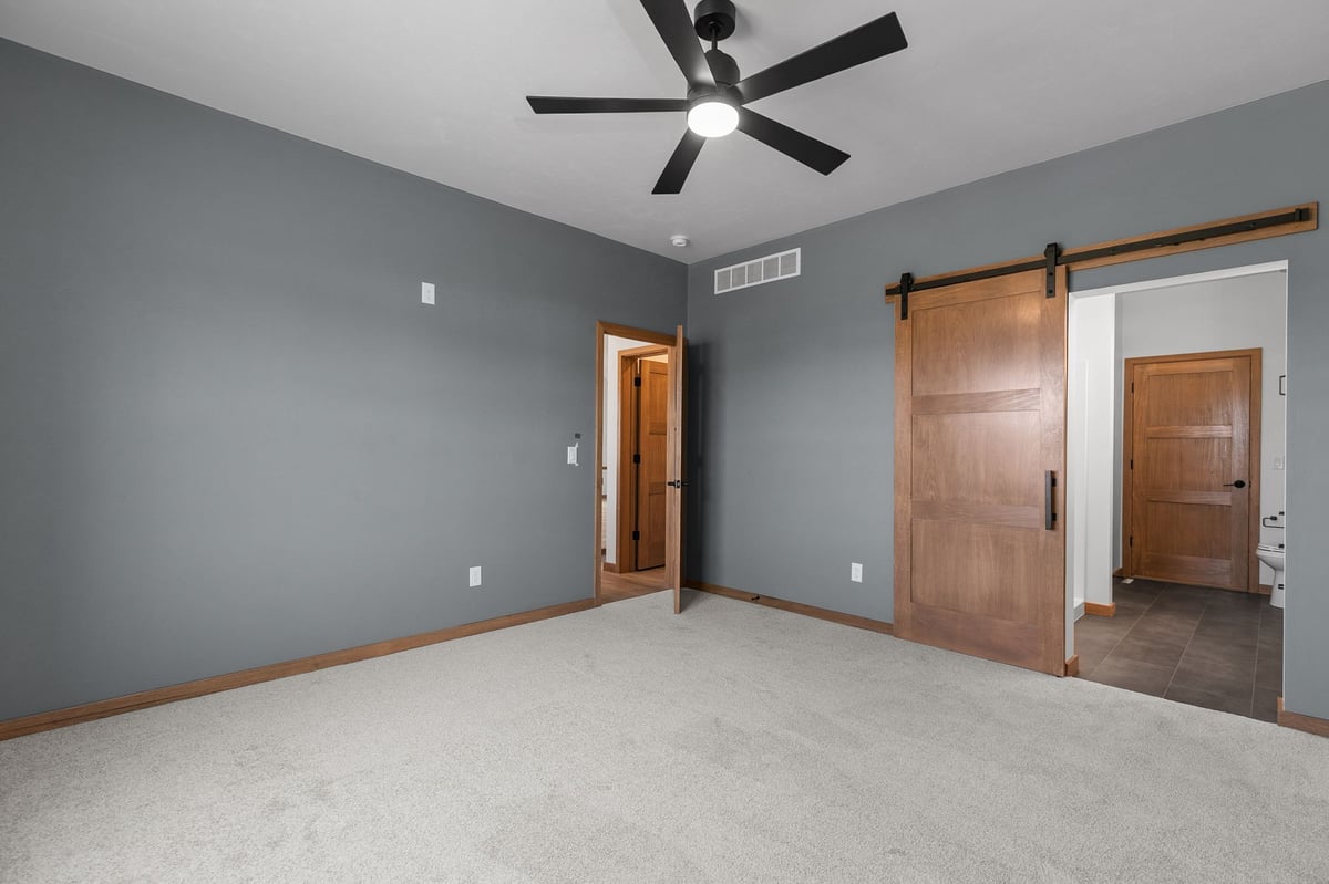 Gray bedroom with barn door closet and ceiling fan in a modern Appleton, WI home