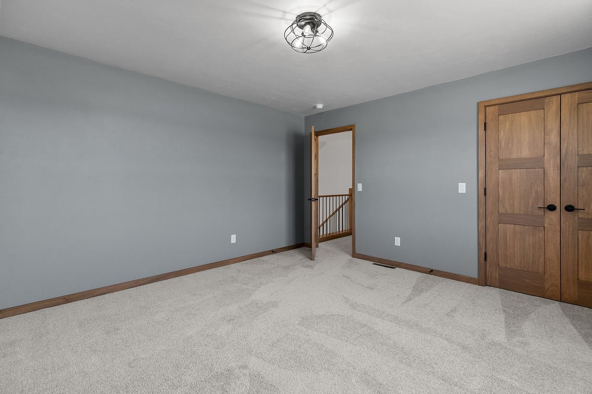 Modern bedroom with gray walls, plush carpet, and wood trim in a newly built Appleton, WI home