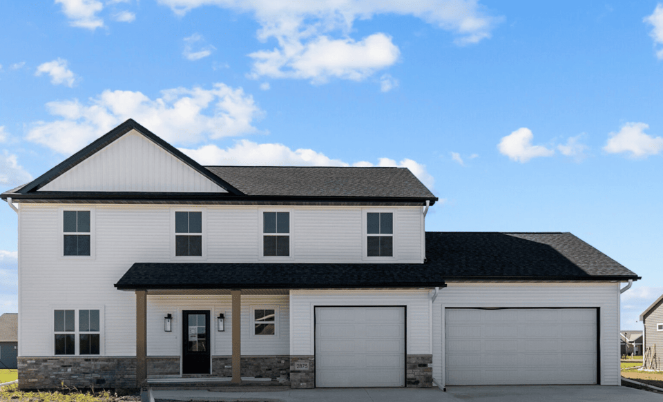 Two-story modern white home in the Fox Cities with black roof, stone accents, and a three-car garage under a bright blue sky